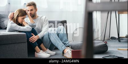 scatto panoramico di bell'uomo calmante giù donna triste in appartamento derubato Foto Stock