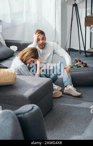 donna triste e uomo scioccato seduto a terra in appartamento derubato Foto Stock