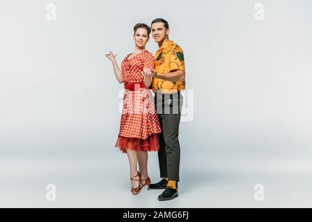 ballerini felici che tengono le mani mentre ballano boogie-woogie su sfondo grigio Foto Stock