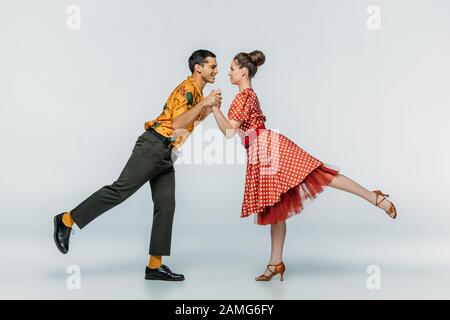 ballerini eleganti che tengono le mani mentre ballano boogie-woogie su sfondo grigio Foto Stock