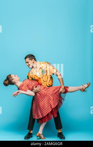bel ballerino che sostiene il partner mentre ballano boogie-woogie su sfondo blu Foto Stock