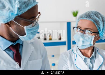 biologi multiculturali in maschere mediche che si guardano l'uno all'altro Foto Stock