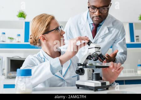 biologi multiculturali in occhiali che guardano al microscopio in laboratorio Foto Stock