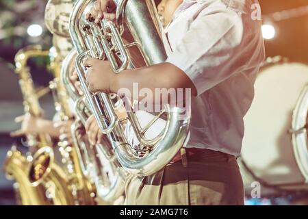 Studente di sesso maschile con gli amici di soffiare il eufonium con la banda per la performance sul palco di notte. Foto Stock