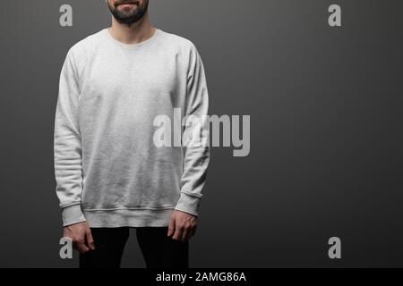 vista dal taglio corto dell'uomo con bearded in una felpa grigia bianca di base su sfondo nero Foto Stock