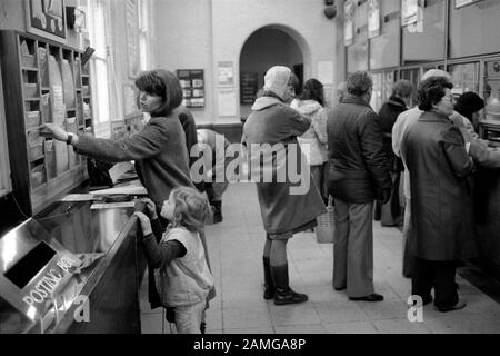 Ufficio postale 1980s Londra UK. Persone che compilano moduli che selezionano volantini. Madre e bambino che vanno all'ufficio postale 1981 HOMER SYKES Foto Stock