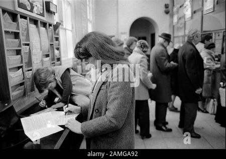 Ufficio postale 1980s Londra UK. Persone che compilano moduli che selezionano volantini. Madre e bambino che vanno all'ufficio postale 1981 HOMER SYKES Foto Stock