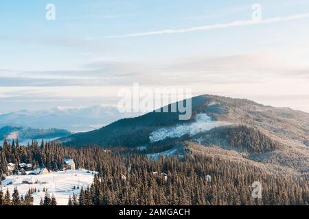 vista panoramica del piccolo villaggio in montagne innevate con pini alla luce del sole Foto Stock