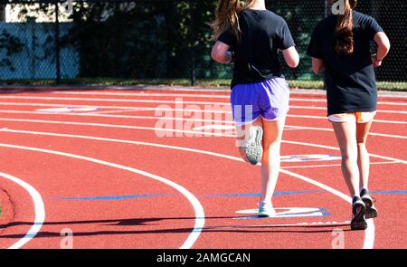 Vista posteriore di due corridori di fondo della scuola superiore che corrono su una pista in due e tre lnes cominciando a girare sulla curva. Foto Stock