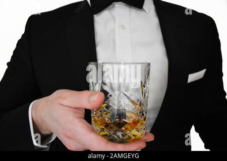 Una vista ravvicinata di un uomo in un tuxedo nero che offre un bicchiere di whisky Foto Stock