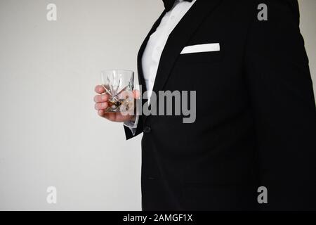 Una vista ravvicinata di un uomo in un tuxedo nero che tiene un bicchiere di whisky Foto Stock