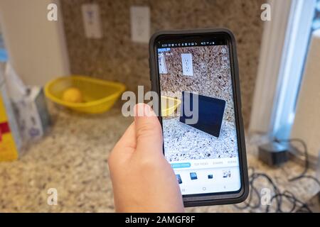 Mano di un uomo che tiene uno smartphone e utilizza le funzionalità di Realtà aumentata nell'app per lo shopping Amazon per visualizzare un dispositivo Amazon Echo Show su un bancone della cucina, San Ramon, California, 22 novembre 2019. La AR viene sempre più utilizzata come caratteristica per i consumatori per visualizzare i prodotti nelle loro case prima di prendere una decisione di acquisto. () Foto Stock