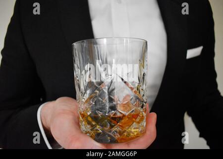 Una vista ravvicinata di un uomo in un tuxedo nero che offre un bicchiere di whisky Foto Stock