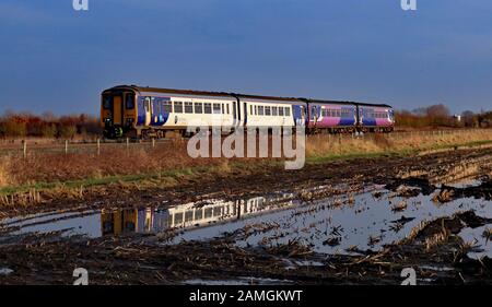 Il giorno di Capodanno 2020 due Nord treni diesel sono riflesse nel bagnare muschio di agricola Burscough moss con un servizio verso il Southport. Foto Stock