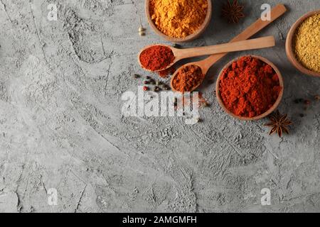 Cucchiai e ciotole con diverse spezie su uno sfondo grigio, vista dall'alto Foto Stock