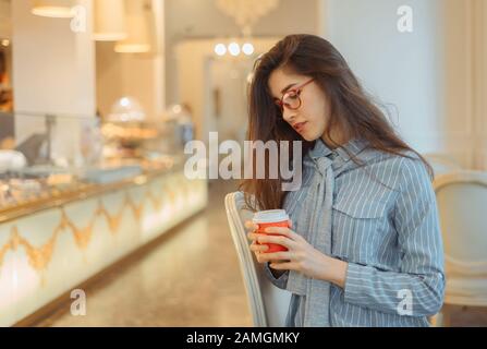 Giovane donna asiatica nel caffè che tiene una bevanda calda in una tazza di carta Foto Stock