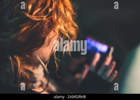 Una ragazza con capelli ricci rossi comunica su uno smartphone. La ragazza corre il dito lungo lo schermo del telefono. Foto Stock