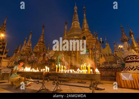 Yangon, Myanmar - 19 dicembre 2019: una donna candela di luce nella parte anteriore della Shwedagon pagoda al crepuscolo. Shwedagon è il più sacro pagoda in Myanmar Foto Stock