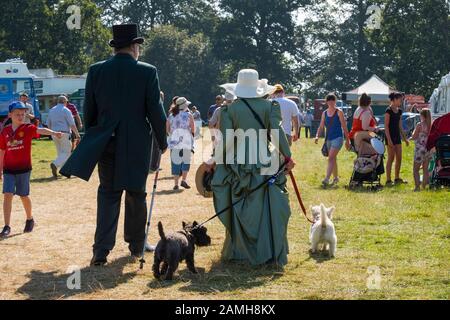 L uomo e la donna in costume a piedi con due cani di 2019 Shrewsbury Rally di vapore, Shropshire, Inghilterra, Regno Unito Foto Stock