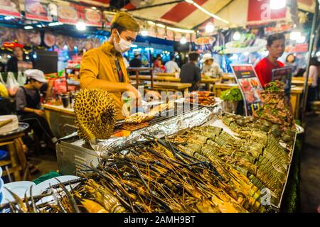 Bangkok/Thailand-05 Dicembre 2019: Scene dal mercato del cibo notturno Talat Rot Fai, aragoste crude su ghiaccio pronte per la vendita con un cuoco sullo sfondo Foto Stock