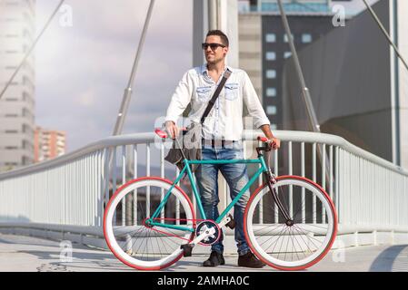 Un giovane uomo elegante in posa accanto alla sua bicicletta. Foto Stock