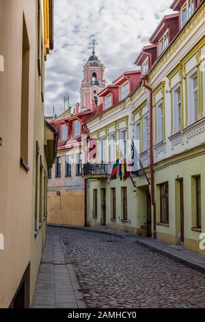 Via della città vecchia, le pittoresche vecchie case con bandiere sopra l'ingresso e il campanile della chiesa cattolica di Tutti i Santi. Vilnius. Lith Foto Stock