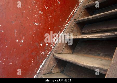 Vecchie scale di legno marrone danneggiato e parete rossa che conduce alla soffitta, ha bisogno di rinnovamento Foto Stock