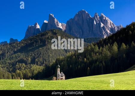 Chiesa di San Giovanni in Ranui, Val di Funes, Alto Adige, Italia con sfondo dolomitico e verde pascolo in primo piano Foto Stock