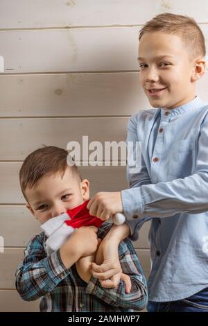 Un ragazzo di 4 anni in una camicia klepy blu grida su uno sfondo di legno chiaro e suo fratello, di 10 anni, è in piedi Foto Stock