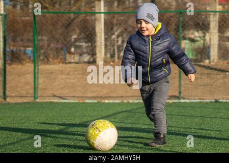 Un ragazzo di 4 anni gioca a calcio con una palla su un campo di erba sintetica Foto Stock