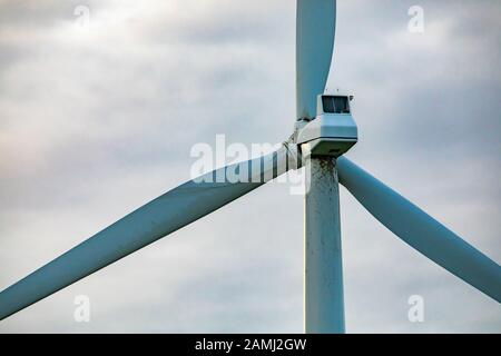 Primo piano dettagli di una torre del convertitore di energia eolica contro un cielo grigio nuvoloso con spazio di copia a sinistra. Che mostra la scatola ingranaggi, il monopolo e tre lame Foto Stock