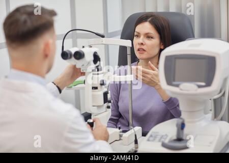 Ritratto di oftalmologo maschile utilizzando rifrattometro oftalmico durante la consultazione con paziente femminile in clinica Foto Stock