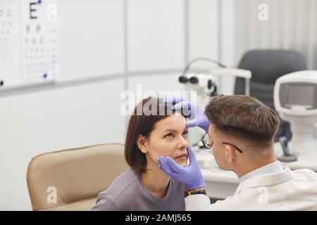 Ritratto ad alto angolo di giovane oftalmologo apertura occhio di paziente femminile mentre controlla la sua visione in clinica farmaco, copia spazio Foto Stock