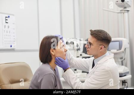 Vista laterale ritratto di giovane oftalmologo apertura occhio di paziente femminile mentre controlla la sua visione in clinica farmaco, copia spazio Foto Stock