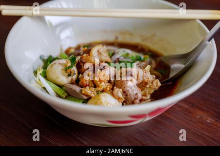 Vista ravvicinata della Speziata zuppa di riso Thai Boat Noodle Soup, Kuai Tiao Ruea, servite su una ciotola di ceramica su un tavolo di legno. Foto Stock