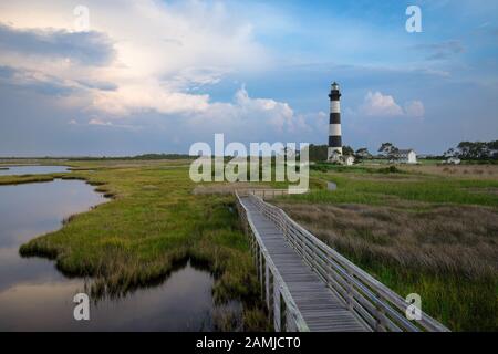 Tramonto al Faro di Bodie Island nelle Outer Banks, Carolina del Nord, con passerella in legno in primo piano sulla palude dell'oceano Foto Stock