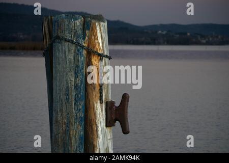 Palo di legno per ormeggio navi contro il lago Trasimeno in background durante il tramonto Foto Stock