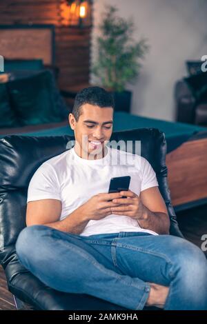 Giovane ragazzo nella sua stanza che guarda uno smartphone. Foto Stock