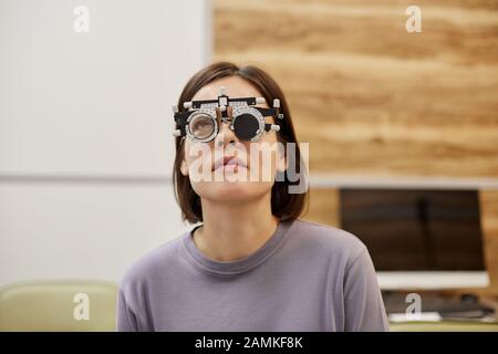 Testa e spalle ritratto di giovane donna che indossa la cornice di prova durante il test di visione in clinica oftalmologia, copia spazio Foto Stock