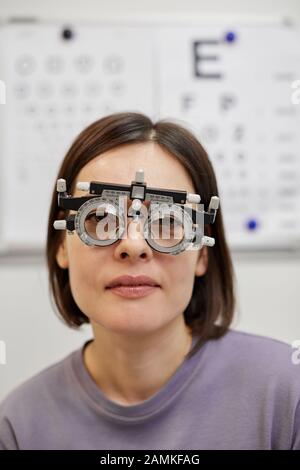 Testa e spalle ritratto di giovane donna che indossa la cornice di prova durante il test di visione in clinica oftalmologia Foto Stock