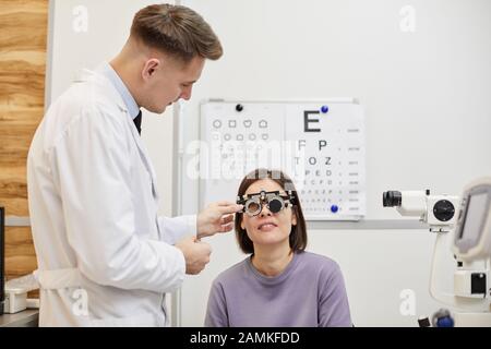 Ritratto del maschio optometristo mettere la cornice di prova su paziente femminile durante il controllo visivo in clinica moderna, copia spazio Foto Stock