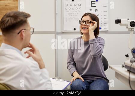 Ritratto di giovane donna entusiasta mettere su nuovi occhiali e sorridere felicemente in oftalmologia clinica, copia spazio Foto Stock