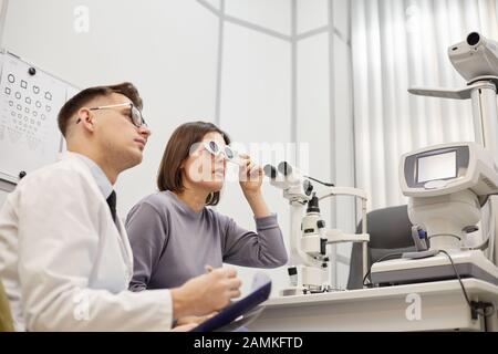 Ritratto di vista laterale di giovane optometristo consulenza giovane donna durante il test di visione in moderna clinica oftalmologia, copia spazio Foto Stock