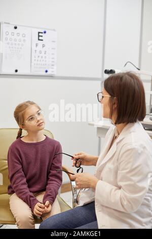 Ritratto di ragazza carina cercando su occhiali durante la prova visiva in moderna clinica oftalmologia, copia spazio Foto Stock