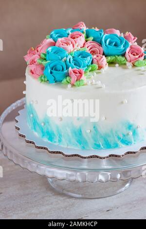 Splendida torta coperta di rose luminose in crema di burro su sfondo di legno chiaro. Foto Stock