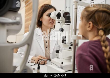 Ritratto di oftalmologo femminile utilizzando rifrattometro mentre si controlla la vista di bambina in clinica moderna, copia spazio Foto Stock