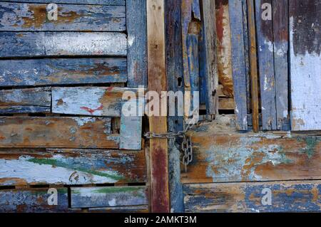 Vecchia porta fatta di tavole di legno, dove la vernice si sfalda. La porta è risettato e le doghe in legno sono dipinte in diverse tonalità di blu. [traduzione automatizzata] Foto Stock