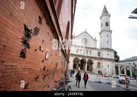 Sulla parete del mattone di costruzione della Monaco Ludwig-Maximilians-University (LMU) all'angolo di Ludwigstraße / Schellingstraße sono buchi pallottole dalla Seconda guerra mondiale. Sullo sfondo il Ludwigskirche. [traduzione automatizzata] Foto Stock