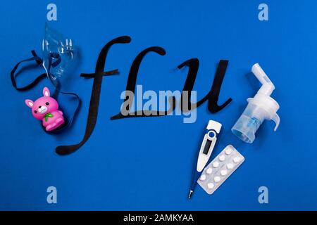 nebulizzatore con maschera per tubo e cavo trasparente tubolare, termometro, compresse e la parola influenza su sfondo blu, raffreddori per bambini. Foto Stock