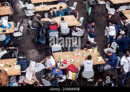 Improvvisato alloggio temporaneo per i rifugiati in una sala espositiva a Riem: Nella foto tavoli e sedie alla distribuzione alimentare per le persone stanche e affamate. [traduzione automatizzata] Foto Stock